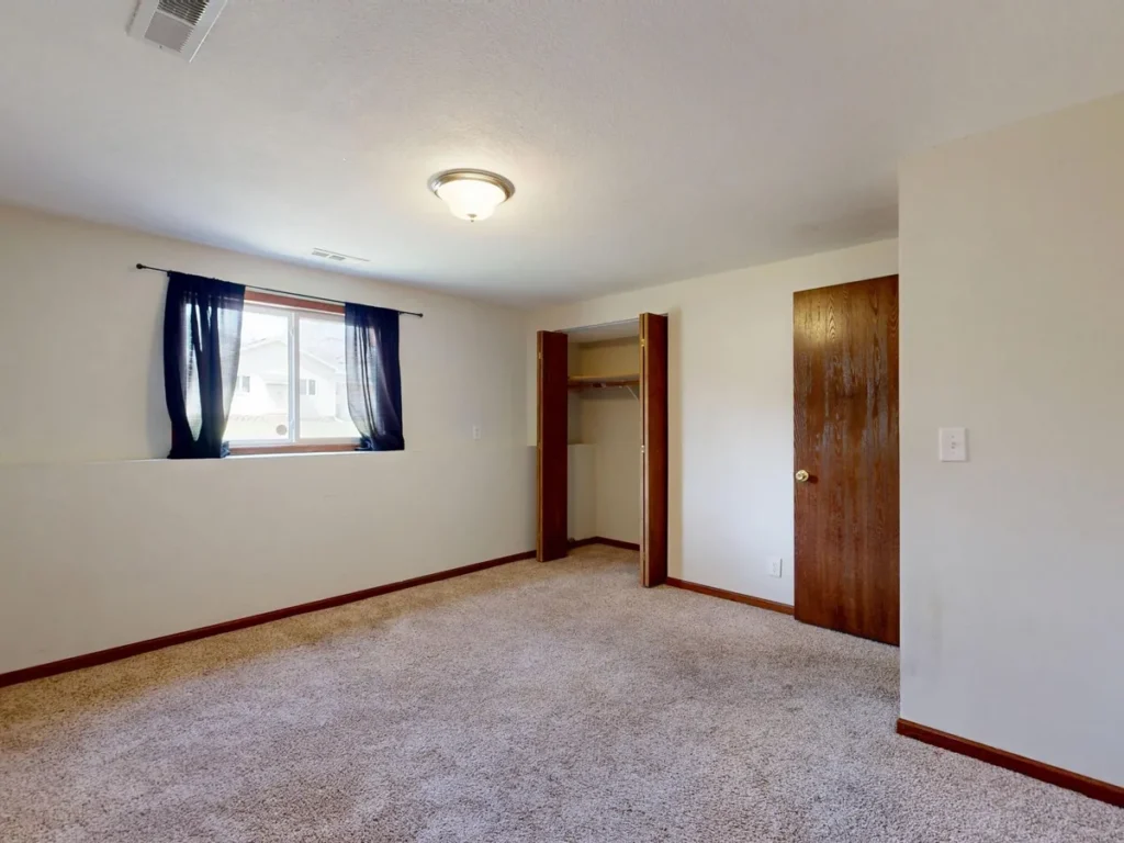 Vacant apartment bedroom with beige carpet, a window and an open closet